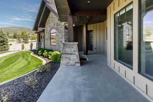 View of exterior entry featuring board and batten siding, a mountain view, stone siding, and a lawn