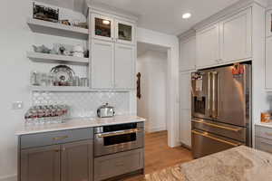 Kitchen featuring stainless steel appliances, tasteful backsplash, light wood finished floors, and open shelves