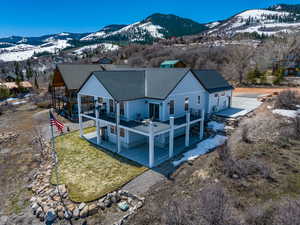 Back of property with a patio area, a deck with mountain view, a shingled roof, and a yard