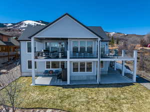 Back of house with a mountain view, a patio, a lawn, and a balcony