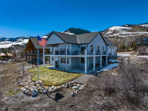 Back of property featuring a balcony, a mountain view, a lawn, a patio area, and a shingled roof
