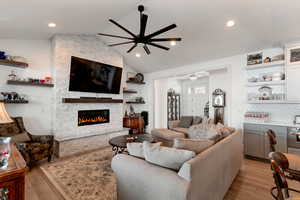 Living area featuring a stone fireplace, recessed lighting, light wood-style flooring, a ceiling fan, and lofted ceiling