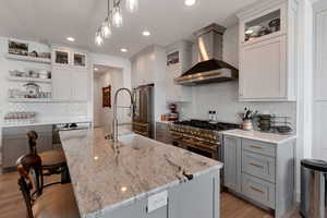 Kitchen with tasteful backsplash, light wood-type flooring, wall chimney range hood, open shelves, and premium appliances