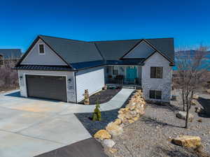 Ranch-style house featuring concrete driveway, a standing seam roof, metal roof, and stone siding