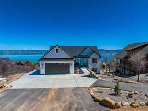 View of front of house with central AC unit, a water view, an attached garage, stone siding, and concrete driveway