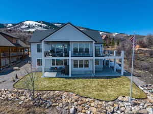 Back of house featuring a mountain view, a lawn, a patio, a balcony, and roof with shingles