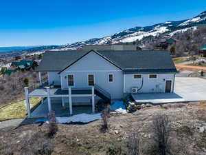 Back of house with a deck with mountain view, stairway, a patio, and roof with shingles