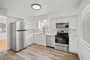 Kitchen featuring light wood-style flooring, a sink, white cabinetry, appliances with stainless steel finishes, and baseboards