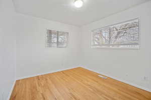 Unfurnished room with plenty of natural light, wood finished floors, visible vents, and baseboards