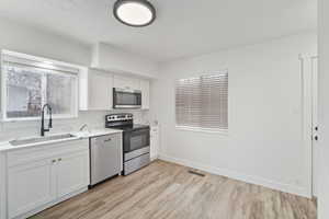 Kitchen with baseboards, a sink, light countertops, appliances with stainless steel finishes, and light wood-type flooring