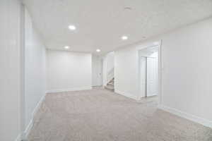 Below grade area featuring stairway, baseboards, light colored carpet, and a textured ceiling