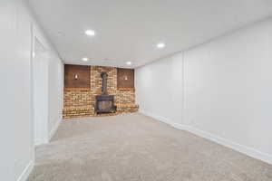 Below grade area featuring a textured ceiling, recessed lighting, carpet, baseboards, and a wood stove
