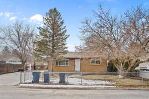 View of front facade with driveway, brick siding, and a fenced front yard