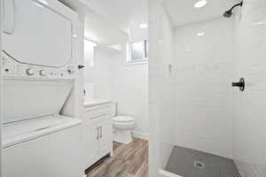 Full bathroom featuring wood finished floors, toilet, a stall shower, and stacked washing maching and dryer