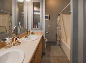 Bathroom featuring double vanity, toilet, wood finished floors, and a sink