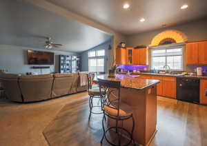 Kitchen with black dishwasher, vaulted ceiling, brown cabinets, a kitchen breakfast bar, and a sink