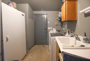 Clothes washing area with light carpet, a sink, cabinet space, and separate washer and dryer