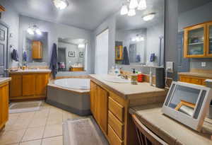 Bathroom featuring a garden tub, lofted ceiling, two vanities, a sink, and tile patterned floors