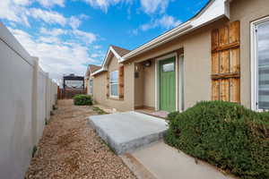 Doorway to property with stucco siding, roof with shingles, and fence