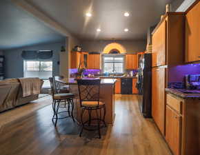 Kitchen with brown cabinetry, black appliances, glass insert cabinets, a kitchen bar, and open floor plan