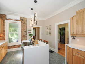 Kitchen with an AC wall unit, brick wall, light countertops, and ornamental molding