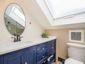 Bathroom featuring lofted ceiling with skylight, toilet, vanity, and tile walls