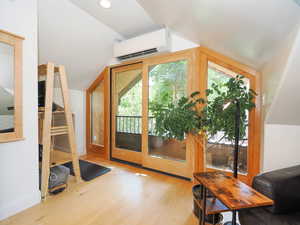 Doorway to outside featuring wood finished floors, a wall unit AC, recessed lighting, baseboards, and vaulted ceiling