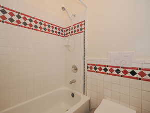 Full bathroom with toilet, tile walls, shower / washtub combination, and wainscoting