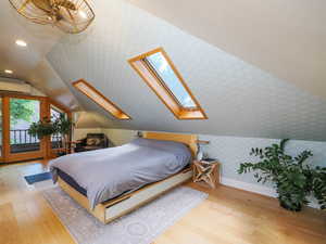 Bedroom with wood finished floors, baseboards, wallpapered walls, lofted ceiling with skylight, and access to outside