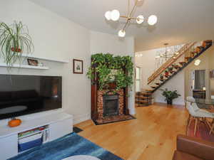 Living room with stairs, wood finished floors, a fireplace, and a chandelier