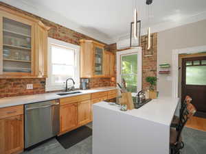 Kitchen with dishwasher, light countertops, a kitchen bar, ornamental molding, and a sink