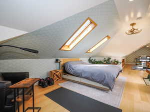 Bedroom with lofted ceiling with skylight, wallpapered walls, and wood finished floors