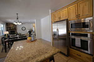 Kitchen with light stone countertops, open floor plan, light tile patterned floors, appliances with stainless steel finishes, and a fireplace