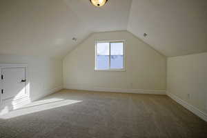 Additional living space with a textured ceiling, lofted ceiling, and light brand new carpet