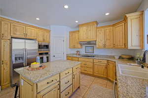 Kitchen with under cabinet range hood, a sink, a kitchen island, recessed lighting, and appliances with stainless steel finishes