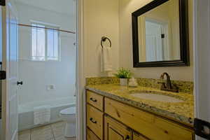 Full bath featuring washtub / shower combination, toilet, vanity, and tile patterned flooring