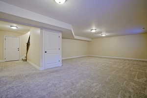 Finished basement featuring a textured ceiling, stairway, baseboards, and light carpet