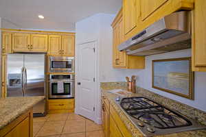 Kitchen featuring under cabinet range hood, light tile patterned floors, stainless steel appliances, and light stone counters