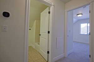 Hall with baseboards, lofted ceiling, light carpet, light tile patterned flooring, and a textured ceiling