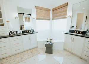 Full bath featuring a bath, marble finish floor, two vanities, and a sink