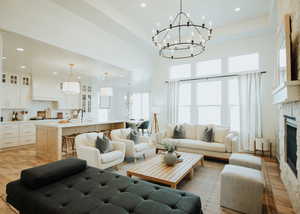Living room with light wood finished floors, a tray ceiling, a stone fireplace, recessed lighting, and a high ceiling