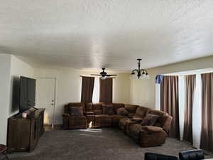 Living area with dark colored carpet, a textured ceiling, and ceiling fan with notable chandelier