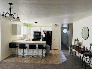 Kitchen with tile patterned flooring, a peninsula, black appliances, and a kitchen bar