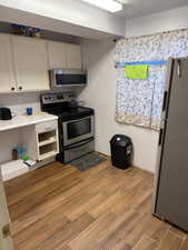 Kitchen featuring stainless steel appliances, wood finished floors, white cabinets, and light countertops