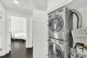 Laundry area featuring recessed lighting, stacked washer and clothes dryer, dark wood-style flooring, and laundry area