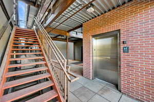 Stairs featuring speckled floor, elevator, and brick wall