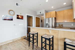 Kitchen featuring light brown cabinetry, visible vents, stainless steel fridge, and a kitchen bar