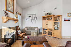 Living room with visible vents, high vaulted ceiling, light wood-style floors, and a glass covered fireplace