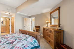 Bedroom featuring visible vents, light carpet, and connected bathroom