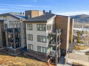 Back of property with a shingled roof, a wall unit AC, a mountain view, and stucco siding